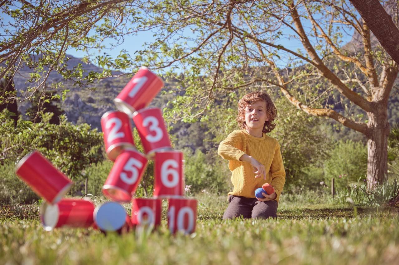 menino brincando de derrubar latas em um espaço aberto e com grama