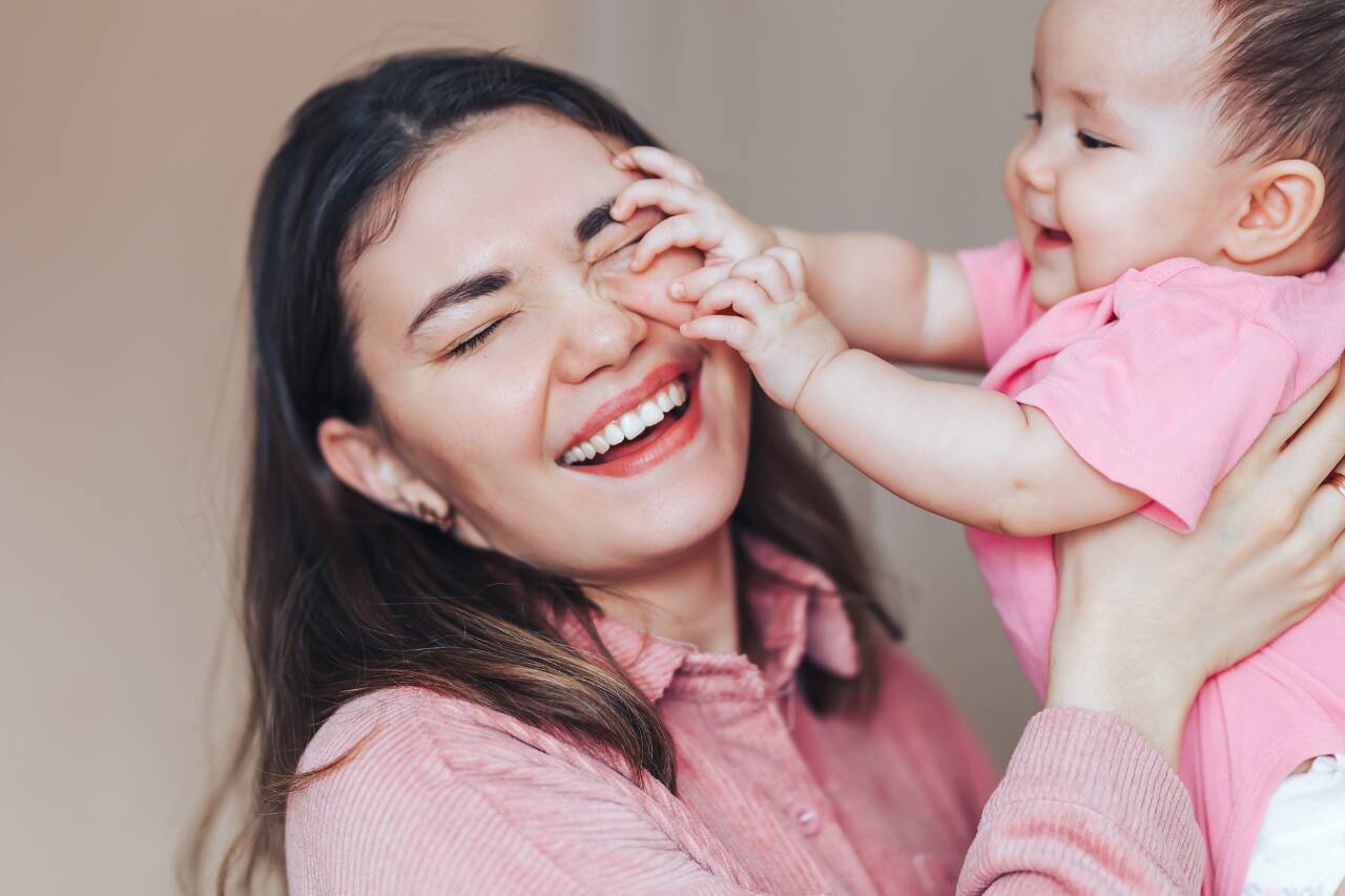 Mãe brincando e sorrindo com bebê alegre.