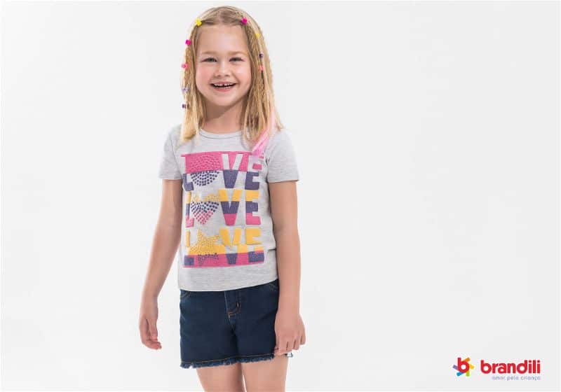 Menina posa para foto com camiseta cinza estampada e short jeans preto