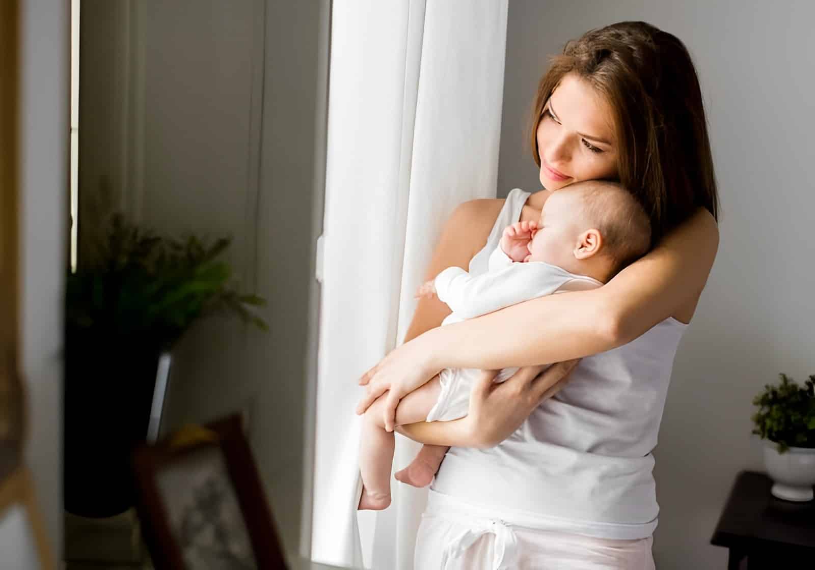 mãe segura o bebe no colo próximo à janela