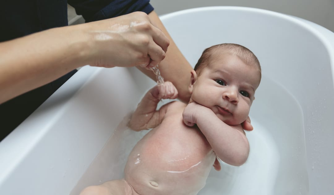 Os cuidados com os recém-nascido. Mulher dando um banho no bebê em uma banheira