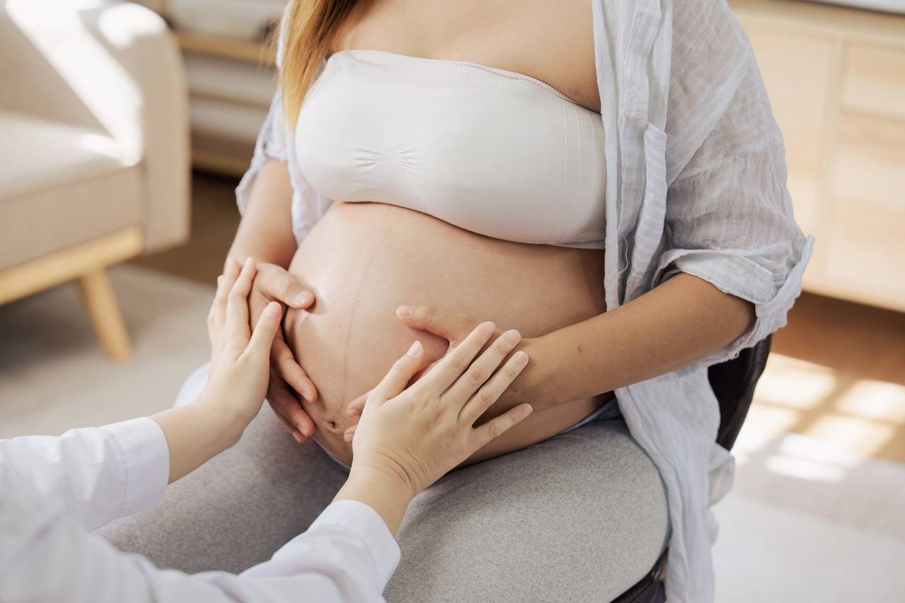 Pessoa tocando barriga de mulher grávida que está sentada em cadeira