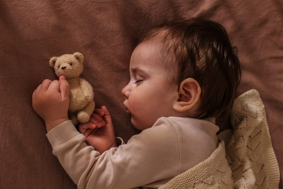 bebê dormindo virada de lado com um ursinho perto 