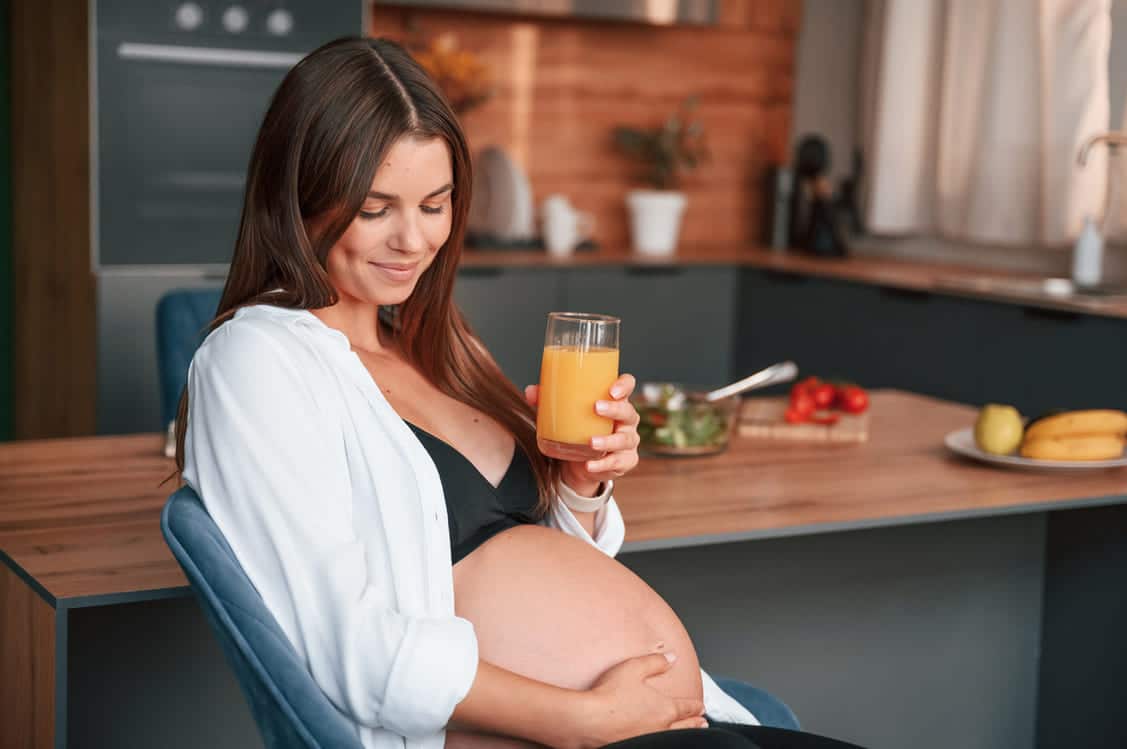 mulher grávida toca a barriga enquanto toma um suco