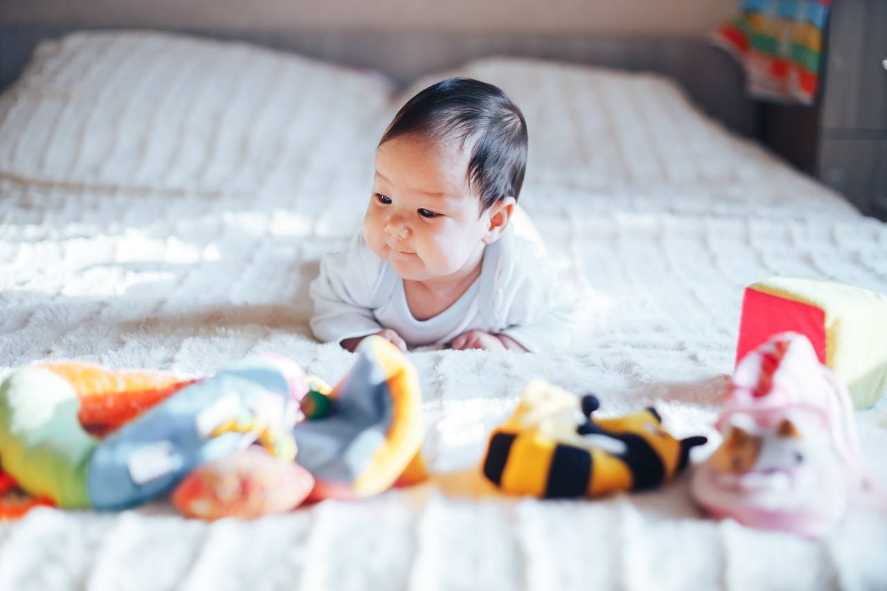 bebê com menos de um ano deitado de bruços na cama dos pais