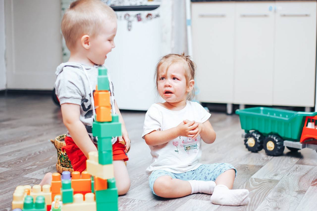 duas crianças de dois anos, um menino e uma menina, brincando no chão da casa