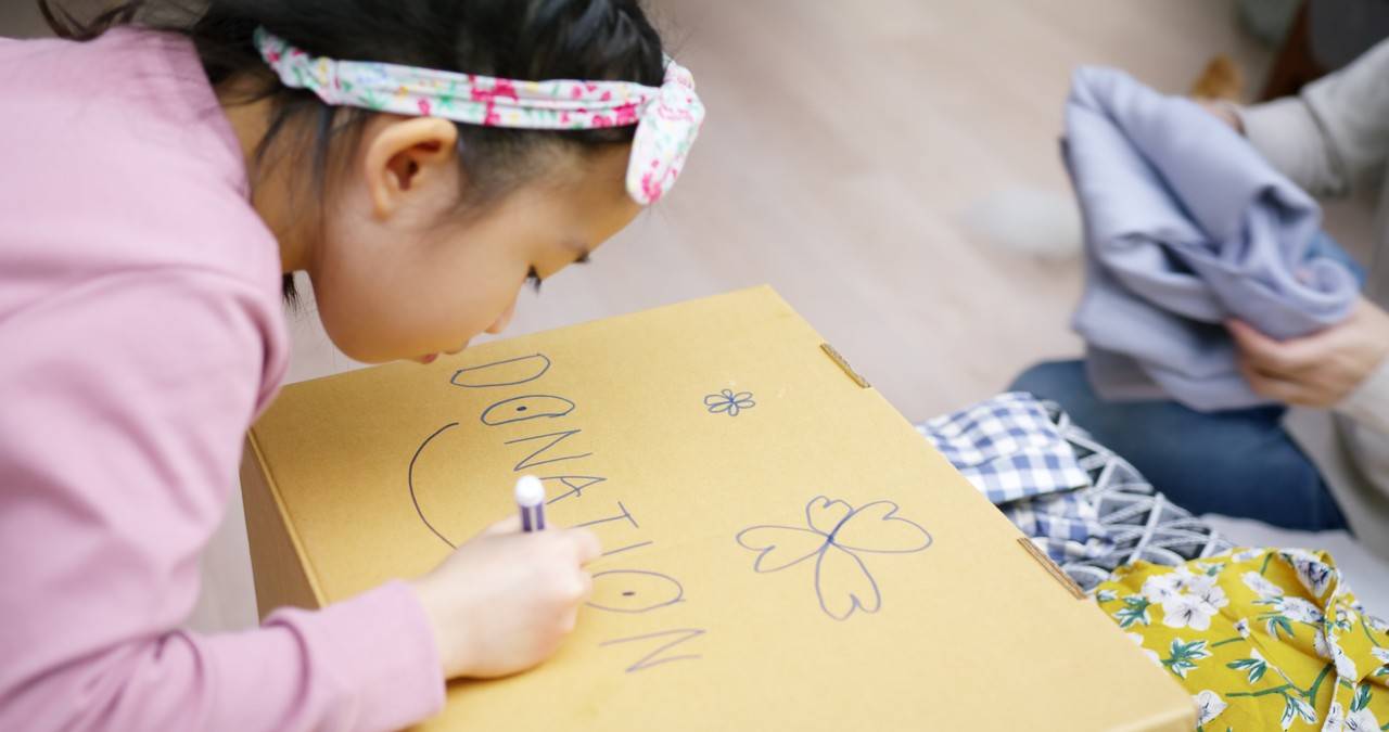 menina escrevendo "doação" em papelão