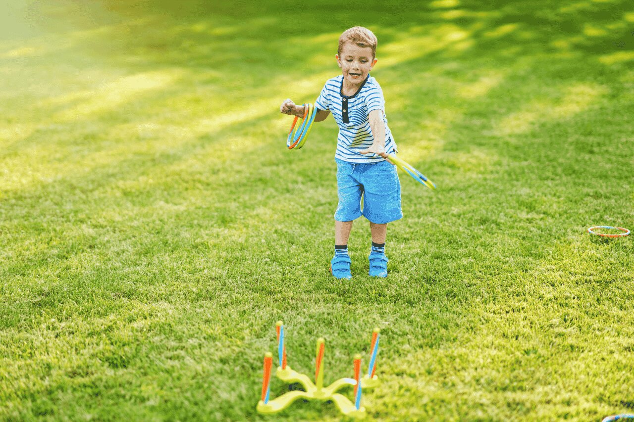 Criança brincando com argolas coloridas no gramado.