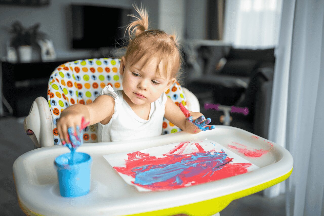 Criança pintando com tinta em mesa de atividades.