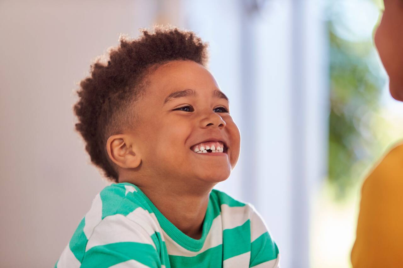 Criança sorrindo com camisa listrada verde e branca.