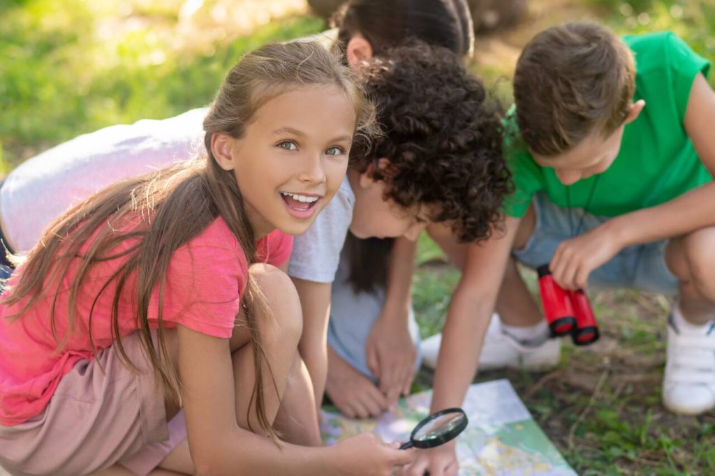 Crianças explorando com mapa e lupa ao ar livre