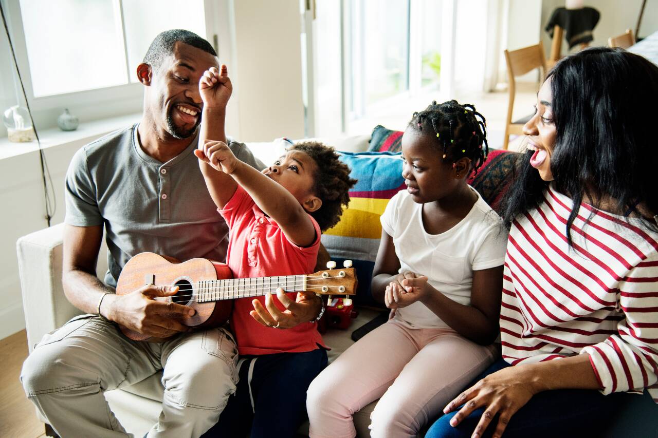 Família sorridente tocando ukulele na sala.
