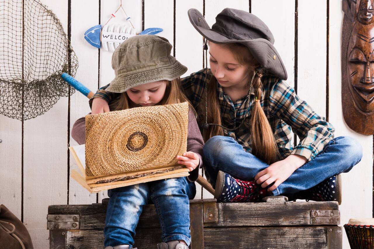Duas meninas explorando um livro em ambiente rústico