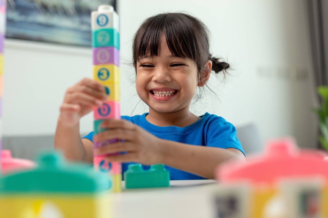 Criança sorridente brincando com bloquinhos coloridos.