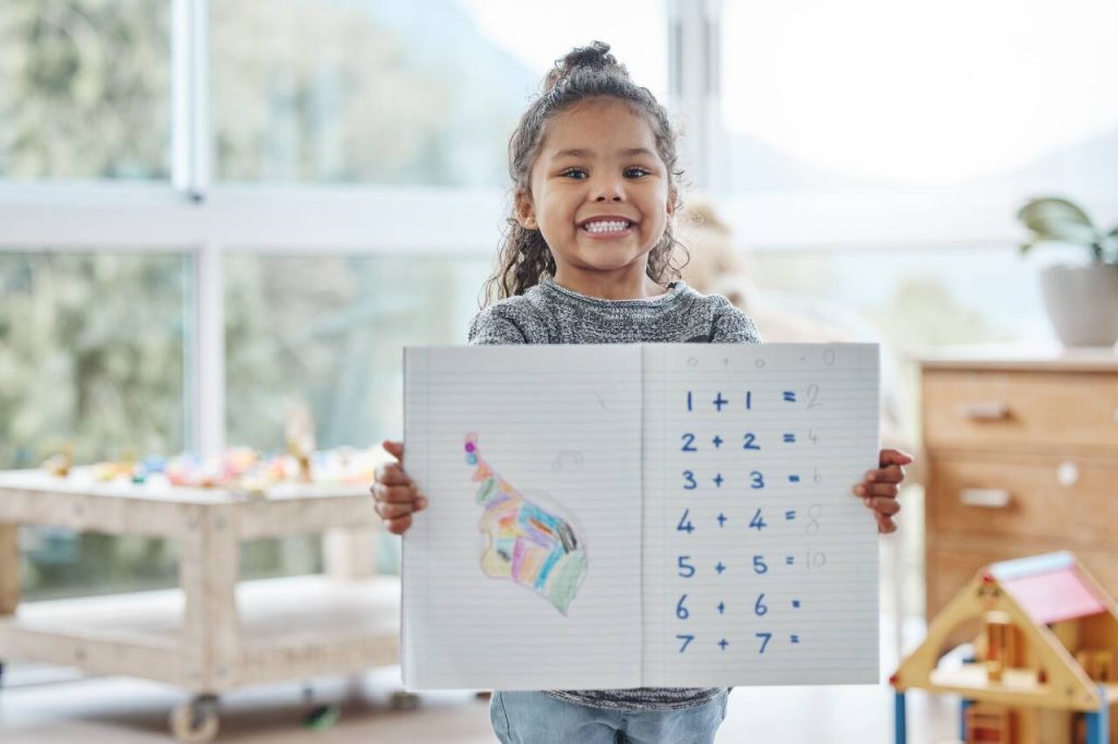 Criança sorridente segurando folha de contas matemáticas
