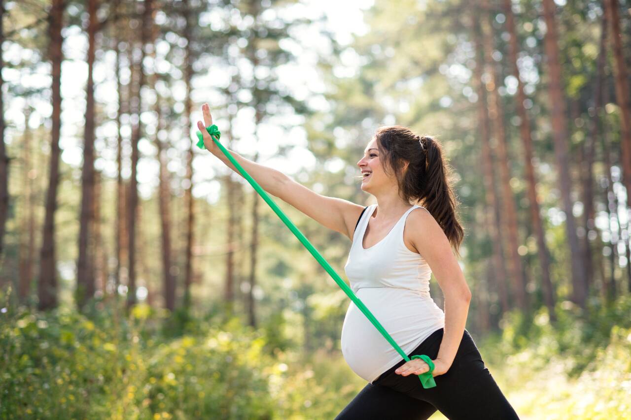 Gestante se exercitando com faixa elástica na natureza