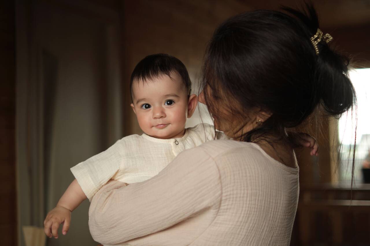 Mãe segurando bebê sorridente em ambiente interno.