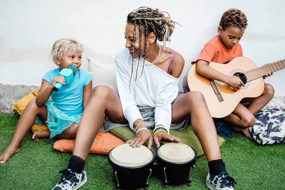Mulher e crianças tocando instrumentos musicais ao ar livre