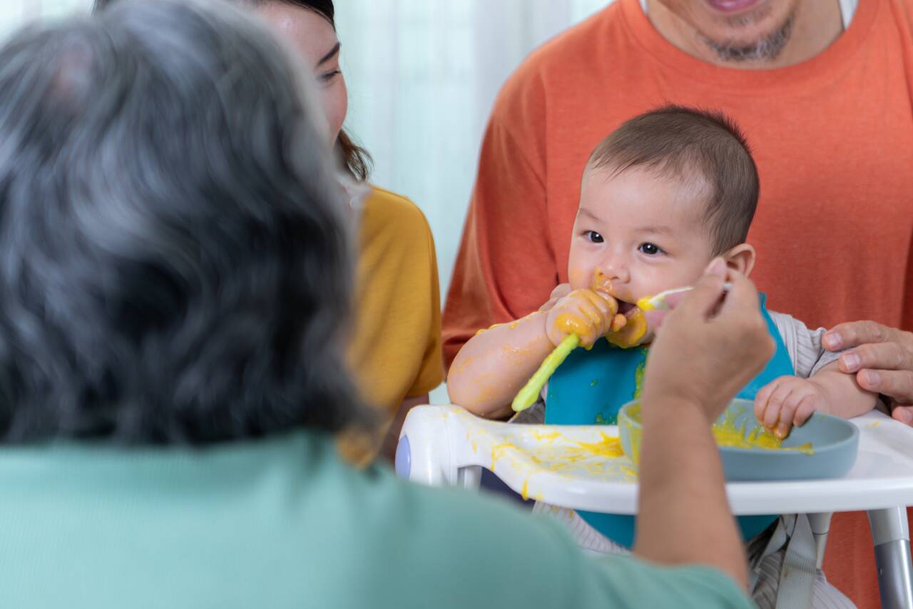 Bebê sentado se alimentando com ajuda familiar