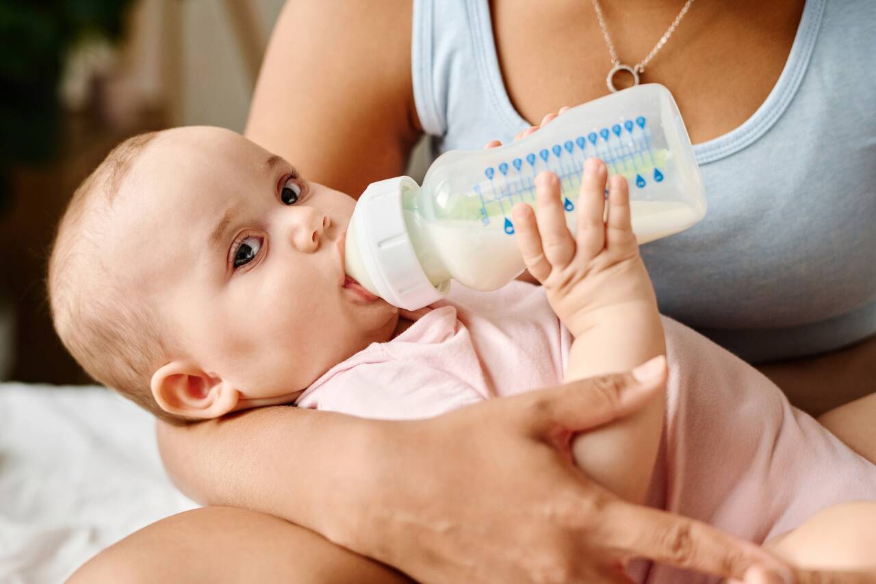 Bebê mamando em mamadeira com carinho.