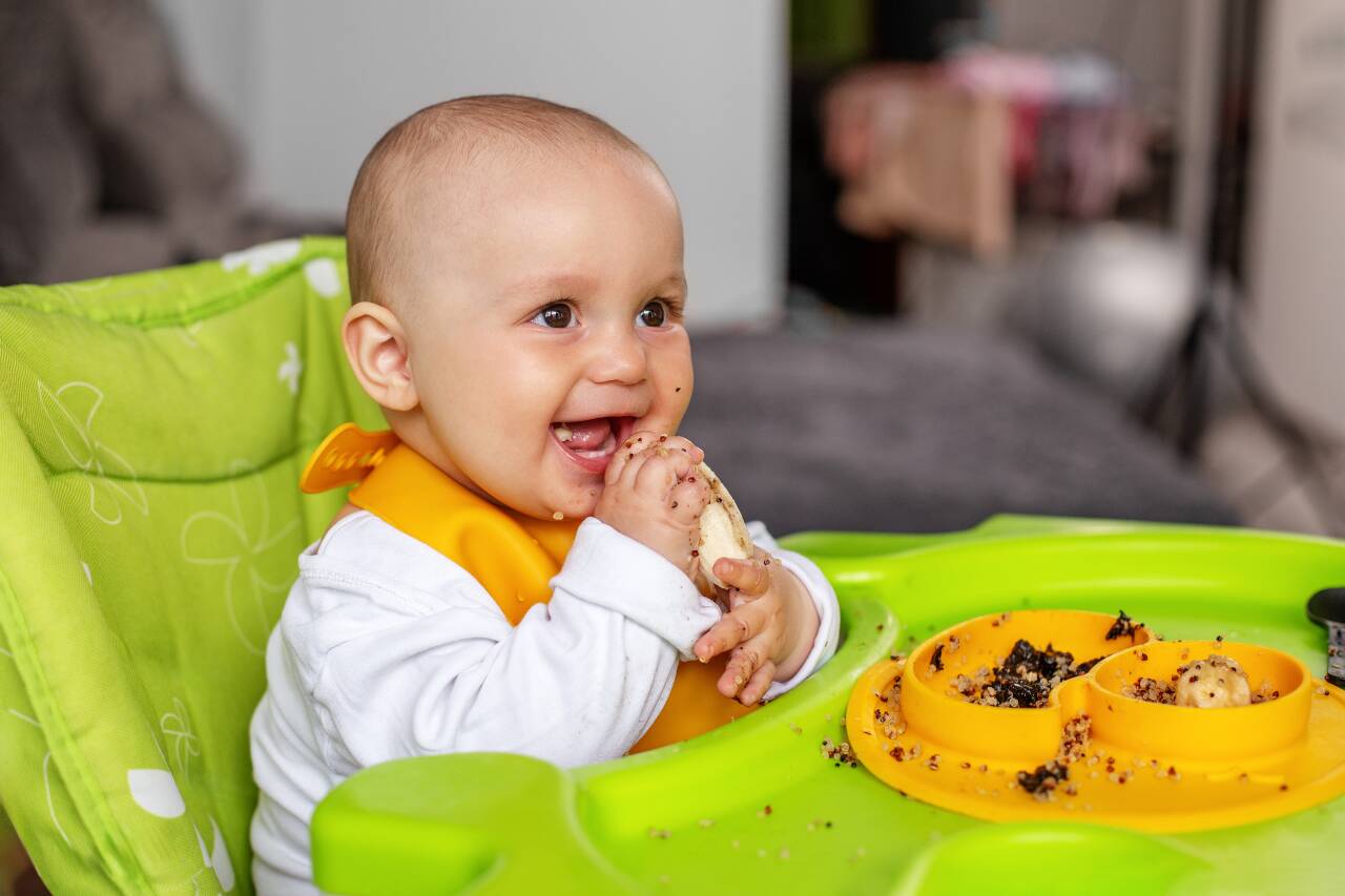 Bebê sorridente comendo e brincando na cadeira alta.