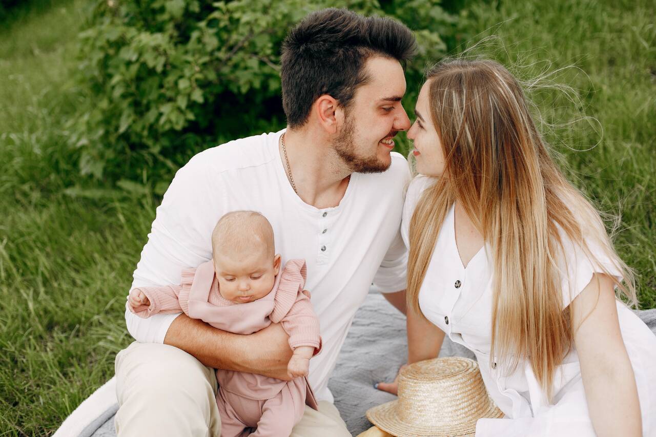 Casal sorrindo com bebê em gramado verde