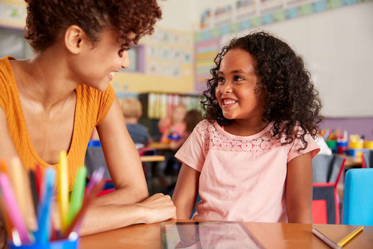 Mãe e filha sorrindo em sala de aula colorida