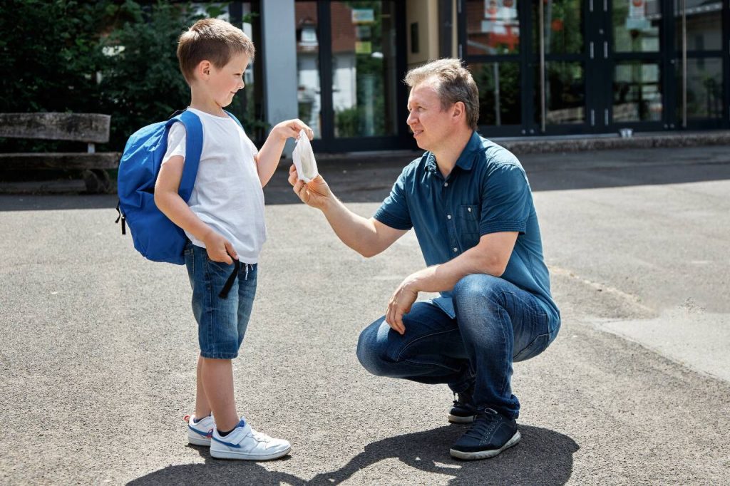 Pai entregando máscara para filho antes da escola