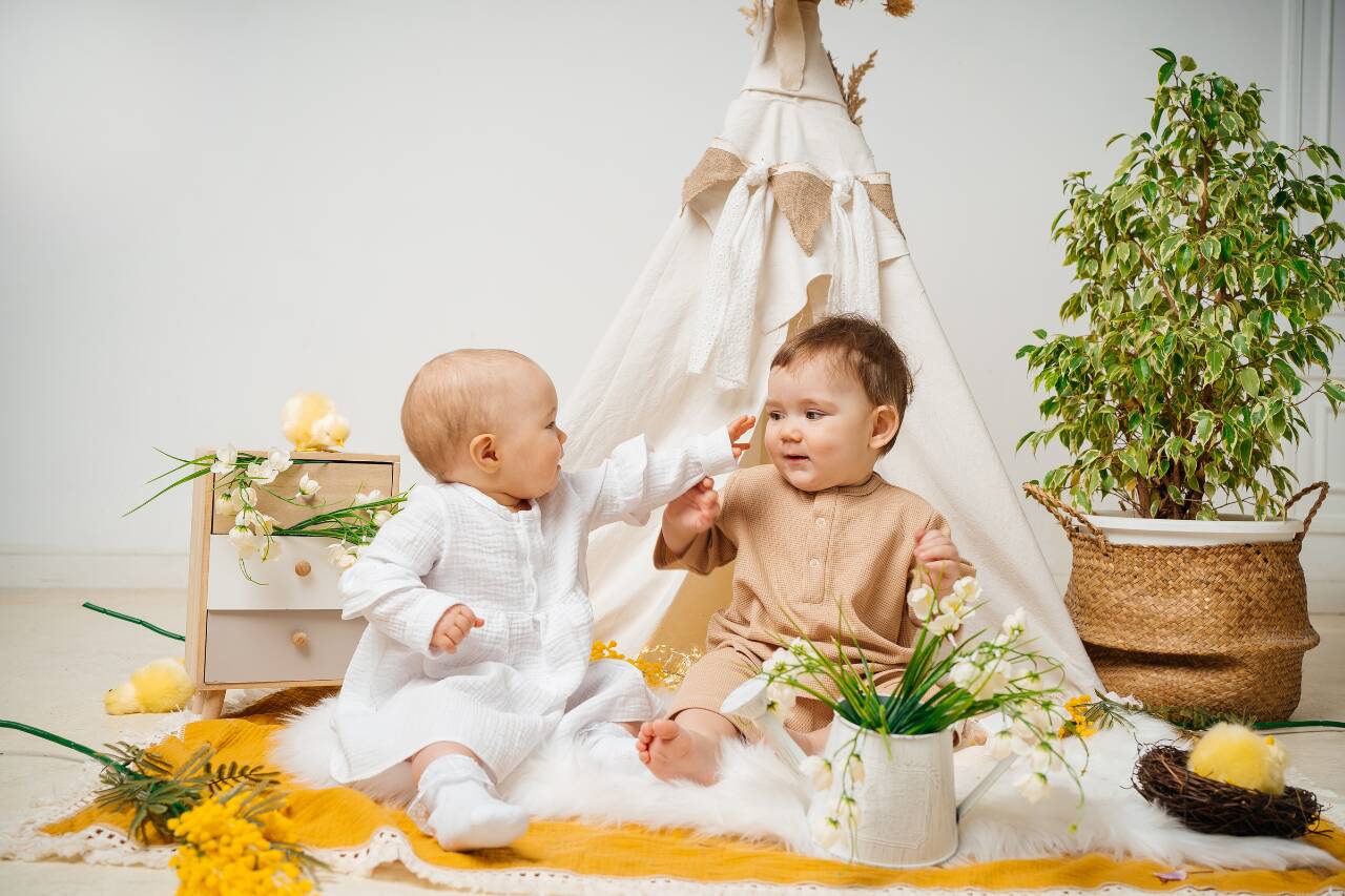Bebês brincando em tenda com flores e decoração alegre.
