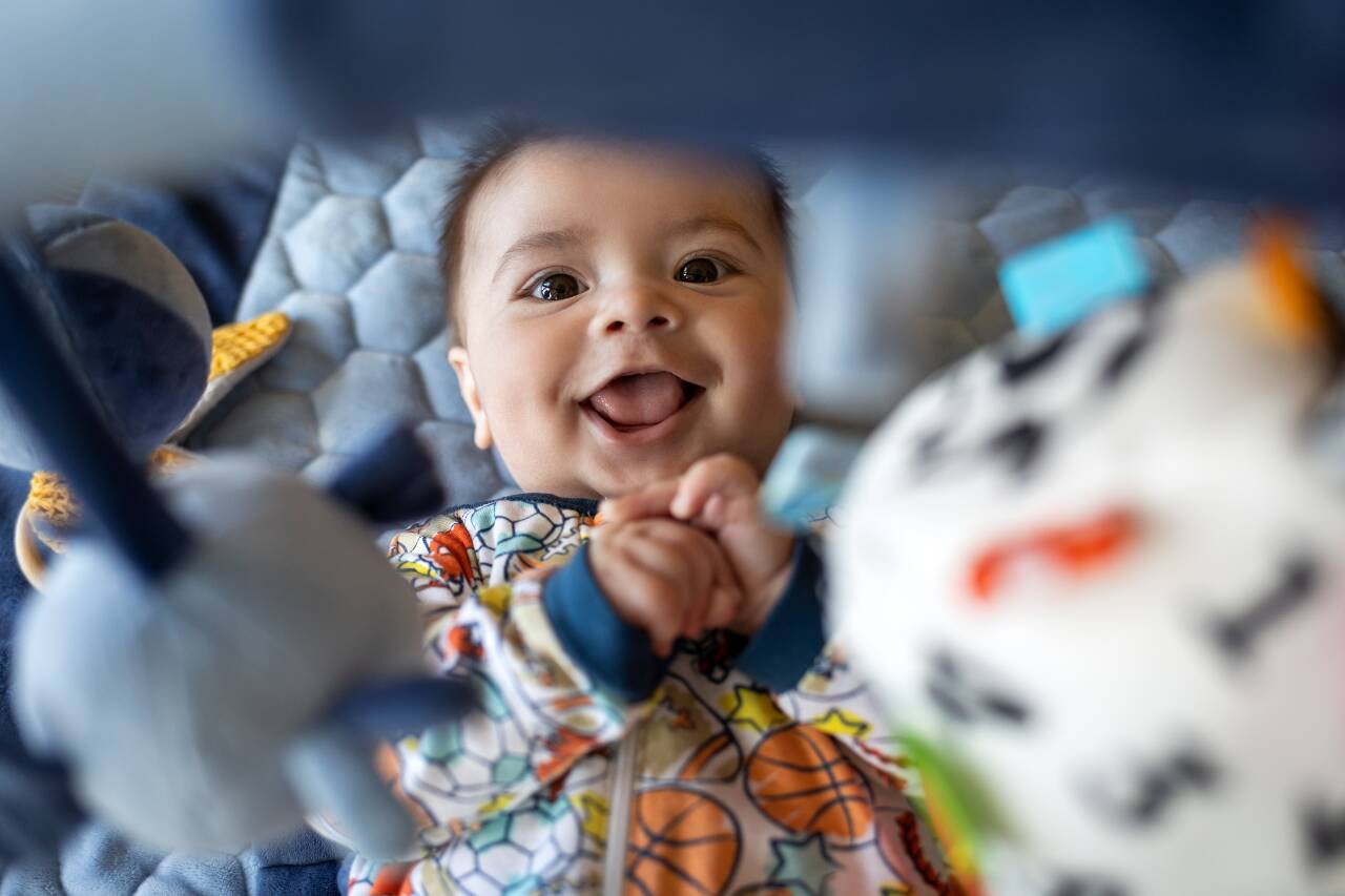 Bebê sorrindo em um tapete de atividades colorido.