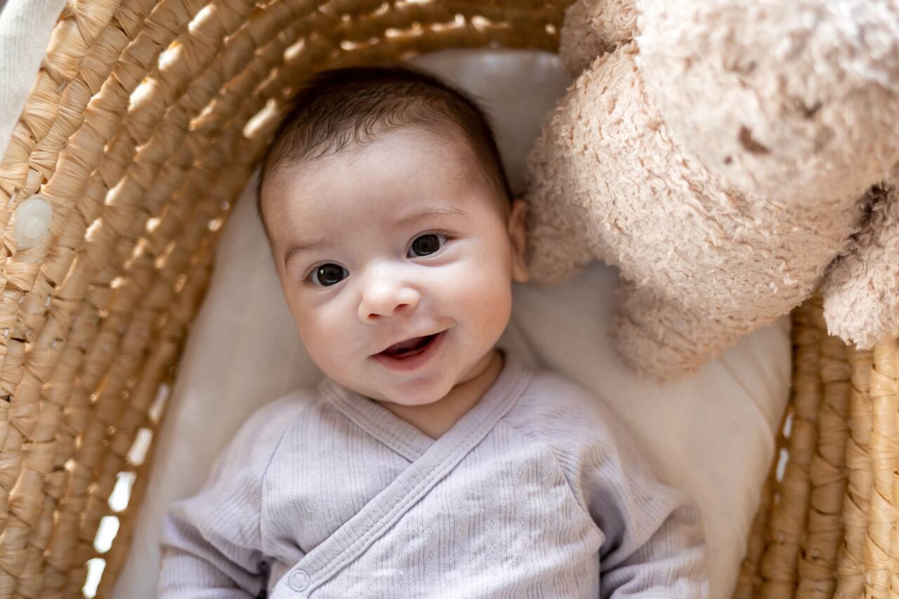 Bebê sorridente em berço com ursinho de pelúcia.