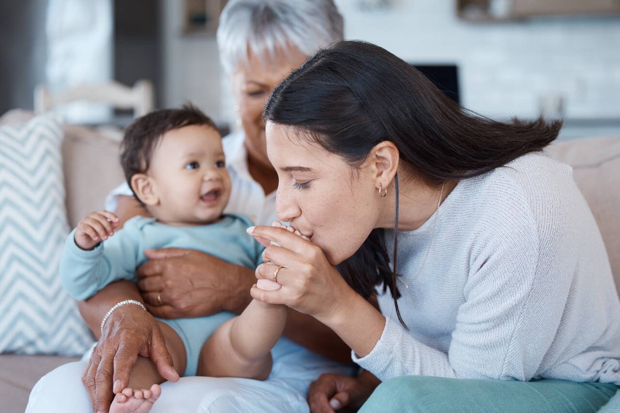 Mãe e avó brincando com bebê sorridente no sofá.